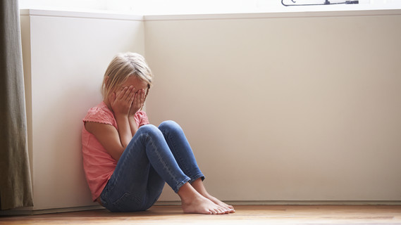 Unglückliches Kind sitzt Zuhause in der Ecke auf dem Boden