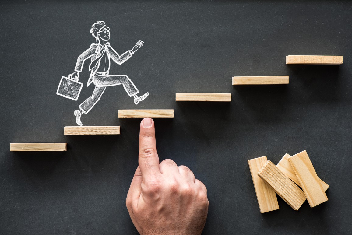 Eine auf einer Tafel gezeichnete Person mit Aktentasche steigt eine Treppe hinauf. Eine Stufe wird von einer Hand an die richtige Position in der Treppe geschoben.