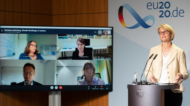 Ministerin Karliczek steht während der Pressekonferenz an einem Pult. Im Hintergrund sind die per Skype zugeschalteten Wissenschaftler zu sehen.