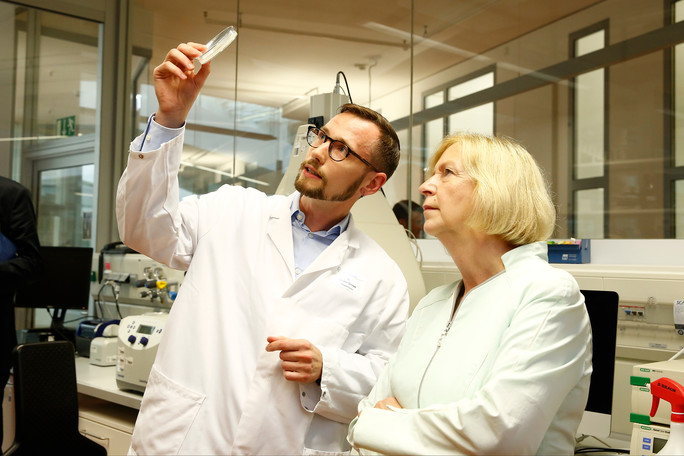 In einem Labor des MPI zeigt ein Mitarbeiter Bundesforschungsministerin Johanna Wanka eine Petrischale mit Rundwürmern