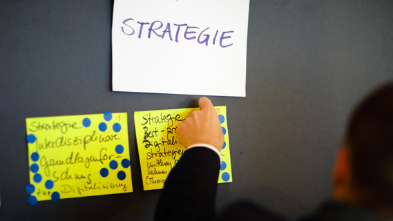 Eine Hand befestigt eine Moderationskarte an einer Pinnwand.