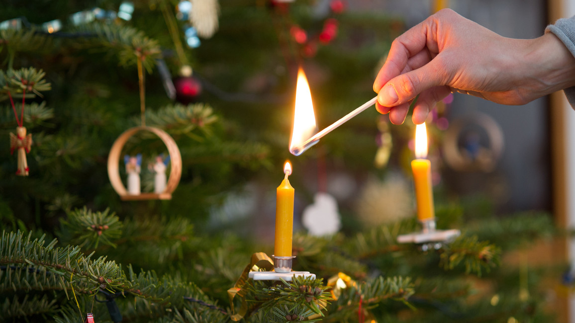 Frau zündet Kerze an Weihnachtsbaum an