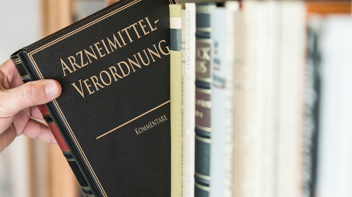 Person zieht das Buch 'Arzneimittel-Verordnung' aus einem Regal