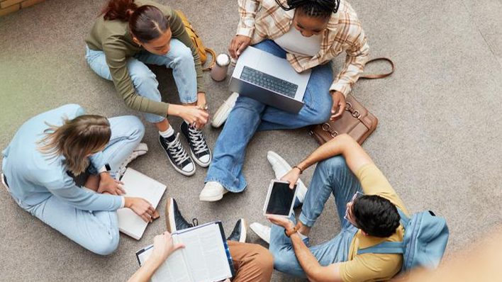 Fünf junge Menschen sitzen in einem Kreis mit Laptop und Notizblöcken.